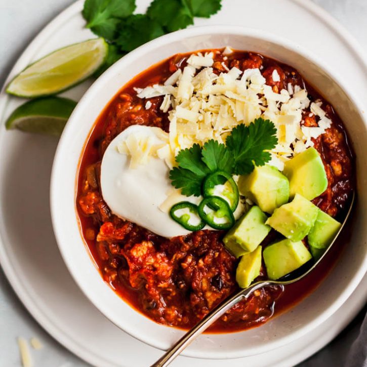 Delicious and healthy slow cooker black bean pumpkin turkey chili garnished with cilantro, sour cream, cubed avocado and shredded cheddar cheese