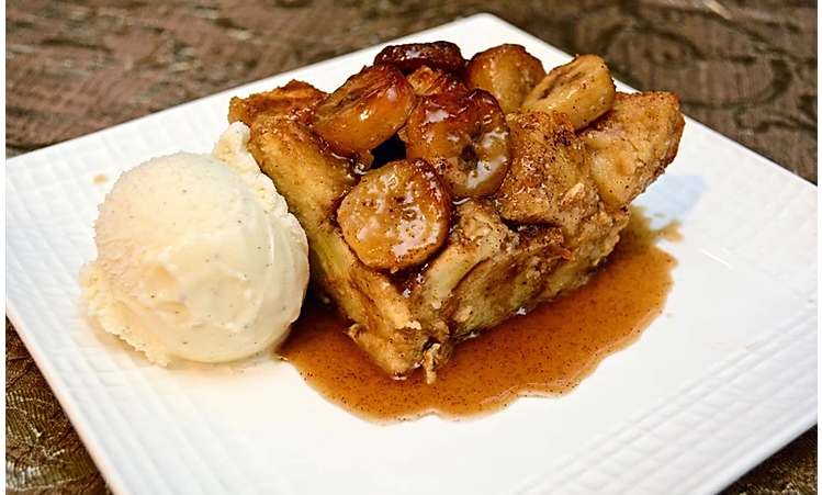 Bananas foster bread pudding served with a small scoop of vanilla ice cream, and drizzled with the rum caramel sauce