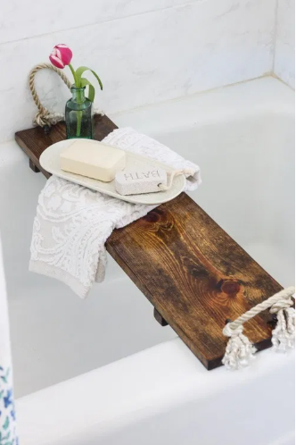 Rustic wood bathtub tray with a flower on vase on it and bath soap