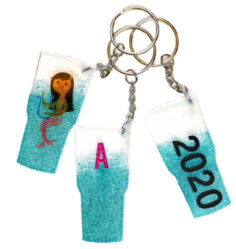 Three resin tumbler keychains, one has a mermaid design on it, second has an letter A on it, the last one has a 2020 design on it.