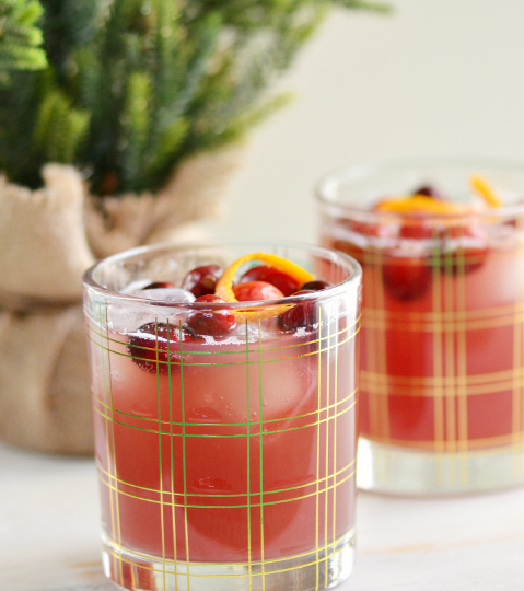 Cranberry pineapple mocktails on a glasses garnished with fresh cranberries and orange peel curls