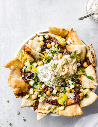 Mediterranean Nachos loaded with toppings and served with hummus and tzatziki