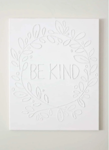 White glue canvas wall art with text saying be kind inside a white circle leaves