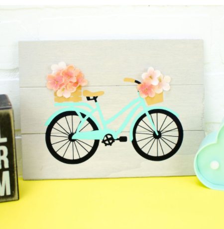 Wooden sign with vinyl die cut of spring colored bicycle, basket on front and back holding flowers