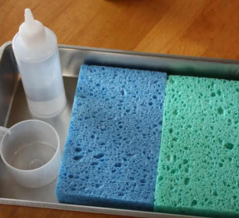 A color blue and green sponge on a pan and a squeeze bottle and measuring cup