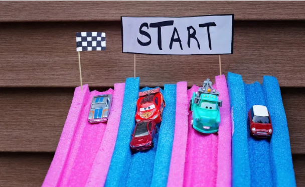Color pink and blue pool noodle racetrack for toy cars with a banner on top that says Start