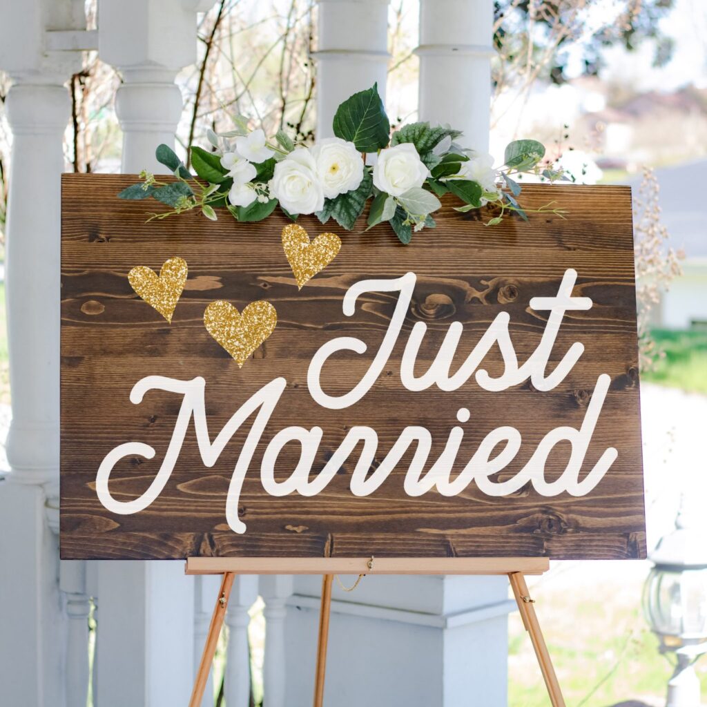 A placa de casamento lindo diz recém-casado com três corações de ouro e uma decoração de rosas brancas acima