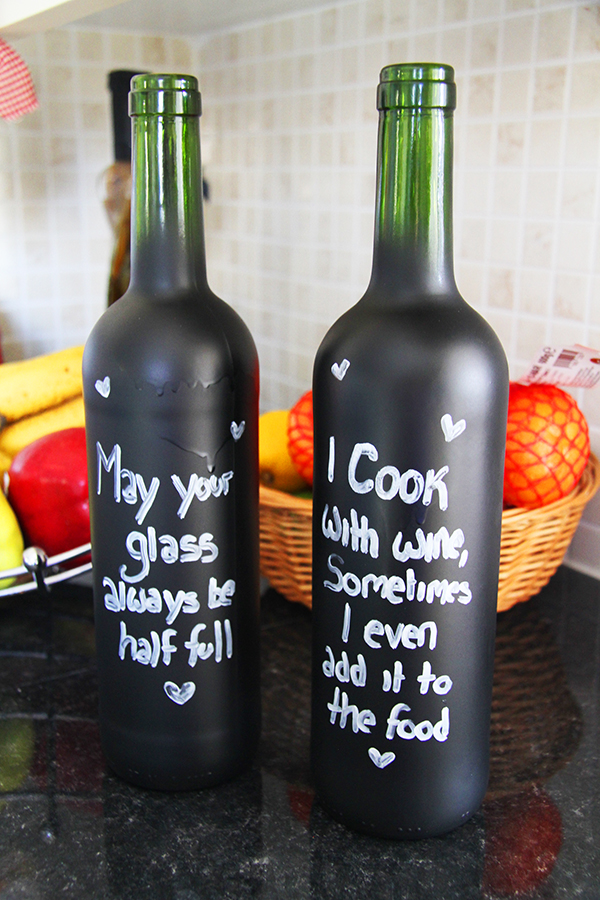 Chalkboard wine bottles. one has a text on it saying May your glass always be half full and a heart details on it, the other one has a text saying I cook with wine, sometimes I even add it to the food