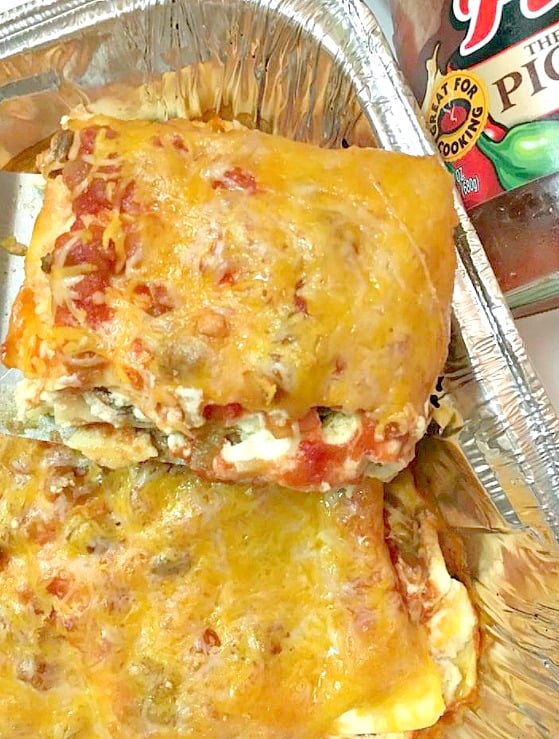 Easy to make taco lasagna top with a dollop of sour cream, chopped green onions, and diced tomatoes.
