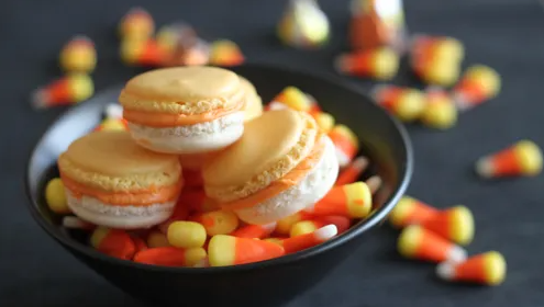 colorful candy corn macaron with a yellow bottom, a white top, and creamy orange pumpkin spice filling