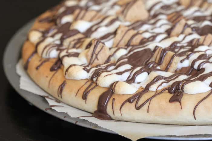Peanut butter s’mores dessert pizza with broken pieces of graham cracker on top and drizzle with melted chocolate